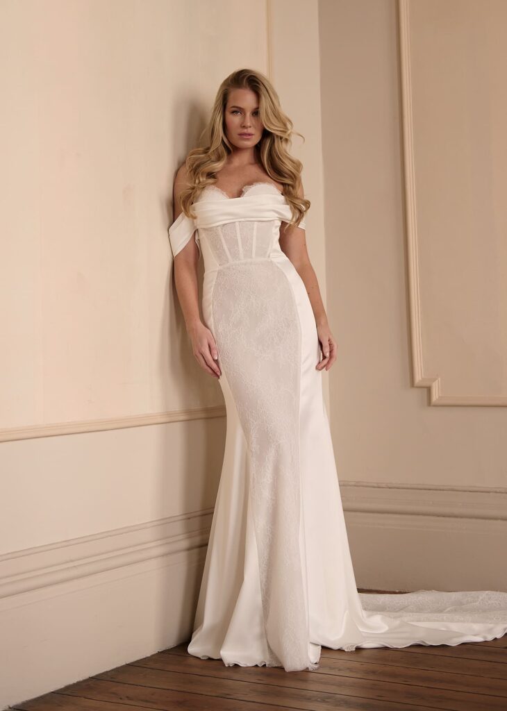 This alluring fit-and-flare gown fuses elegance with sensuality. Featuring a corset-inspired bodice, off-the-shoulder satin draping, and lace paneling through the skirt, it accentuates every curve while maintaining a sophisticated silhouette.