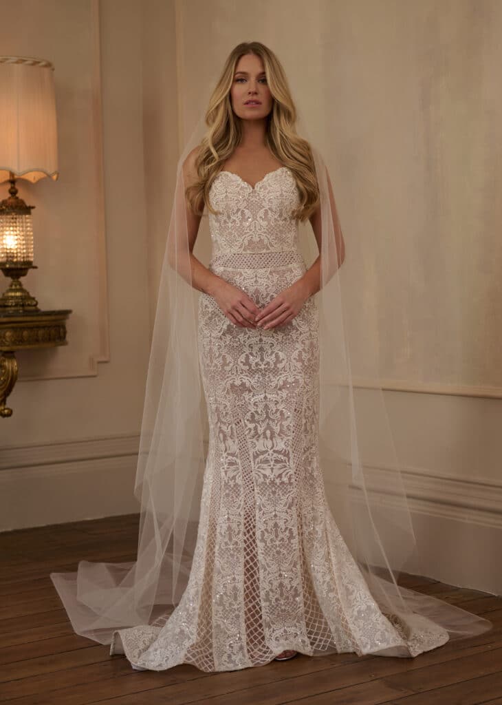 This gown is an exquisite blend of classic romance and refined detailing. Featuring all-over ornate lace with subtle sparkle, this strapless fit-and-flare silhouette hugs the body before flaring softly at the hem.